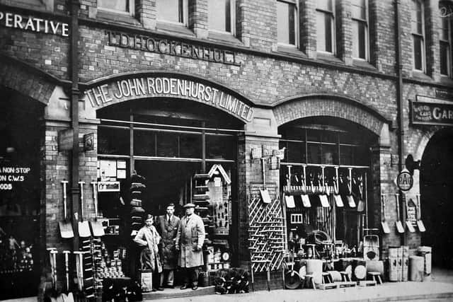 The premises in Market Drayton of 'The John Rodenhurst Limited.' It looks like an ironmongers. Written above is 'T.D. Hockenhull.' Glimpsed far right is a garage and there is also an RAC sign. The people standing outside will be the staff/shopkeeper. The back of this print is completely blank. Possibly taken around 1914. Glimpsed on the left is what we know from another picture is Silverdale Cooperative Society. If we were able to look further up on the facade of this building we would see the wording Raven Foundry and General Implement Warehouse. 