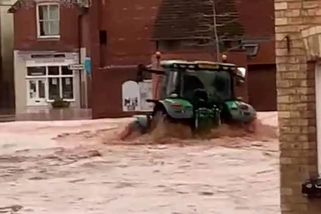 A man in a tractor driving down Tenbury Wells high street creating waves that hit shops