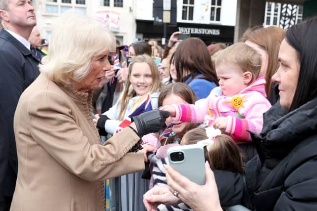 Queen Camilla holds a toddlers hand.