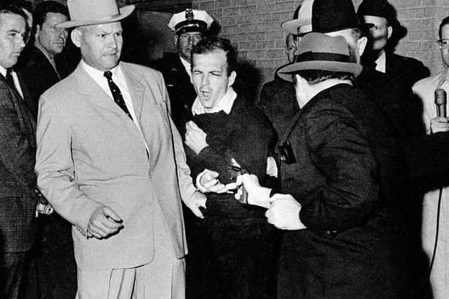 Lee Harvey Oswald, suspected assassin of President Kennedy, grimaces as he is shot at point-blank range by nightclub owner Jack Ruby in the basement of the Dallas police headquarters