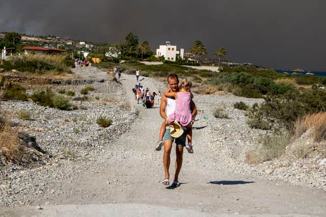 A man carries a child as they leave an area where a forest fire burns, on the Greek island of Rhodes. Photo: Lefteris Diamanidis/InTime News via AP.