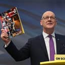 John Swinney holding up a copy of the SNP manifesto
