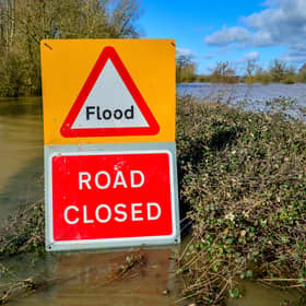 A warning sign highlighting a road closure due to flood, with floodwater visible in the background
