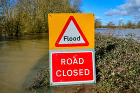 A warning sign highlighting a road closure due to flood, with floodwater visible in the background