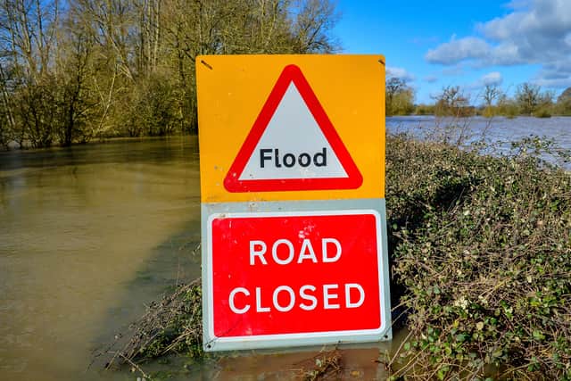 A warning sign highlighting a road closure due to flood, with floodwater visible in the background