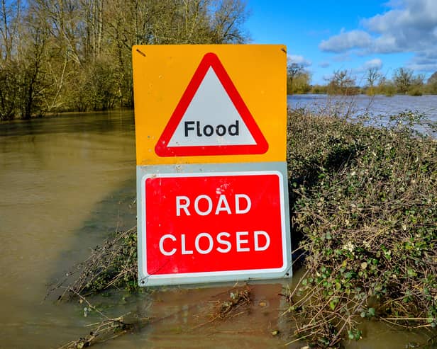 A warning sign highlighting a road closure due to flood, with floodwater visible in the background