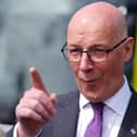 John Swinney points while speaking to journalists