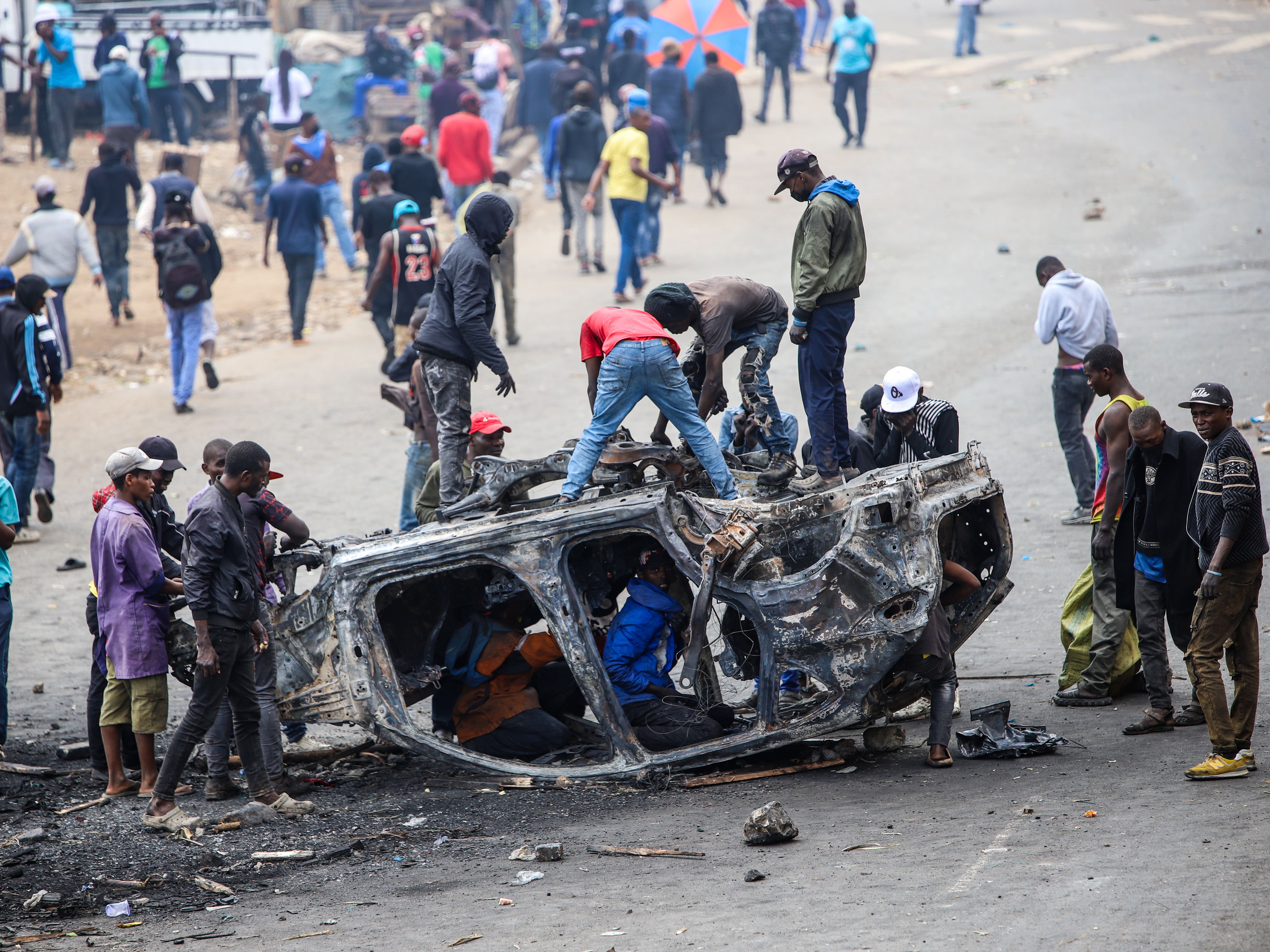 People strip parts from a burned-out vehicle during a public transport strike over fuel prices in Nairobi, Kenya