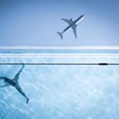 A woman swims in a clear pool while above an airliner flies past, both viewed from below