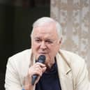 John Cleese with a microphone on stage