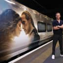 Sam Heughan in front of a train with an Outlander wrap