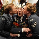 Alec Penstone in Navy uniform being kissed on both cheeks by two women in uniform