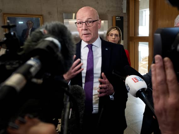 John Swinney speaking in front of a series of microphones and cameras