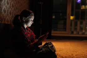 Side view of a young girl sitting on a bed in a dark bedroom looking at her phone