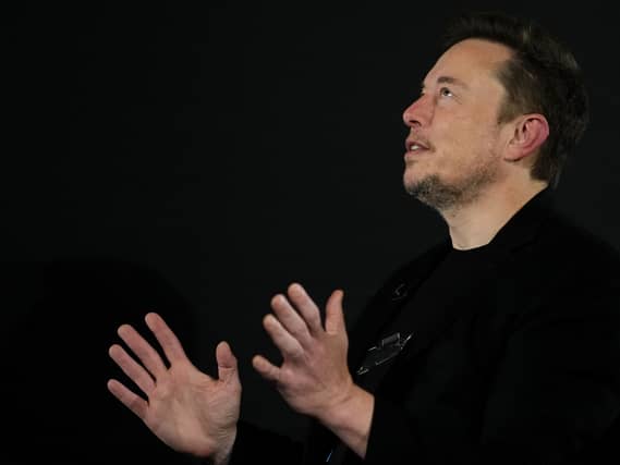 Elon Musk looking upwards and gesturing with his hands