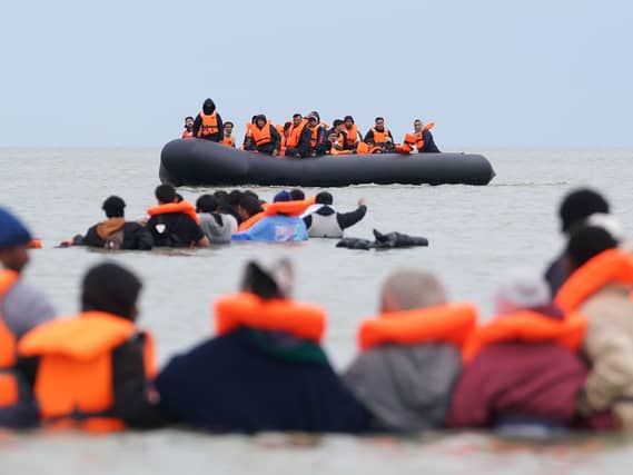 People thought to be migrants wade in the water as they attempt to board a small boat