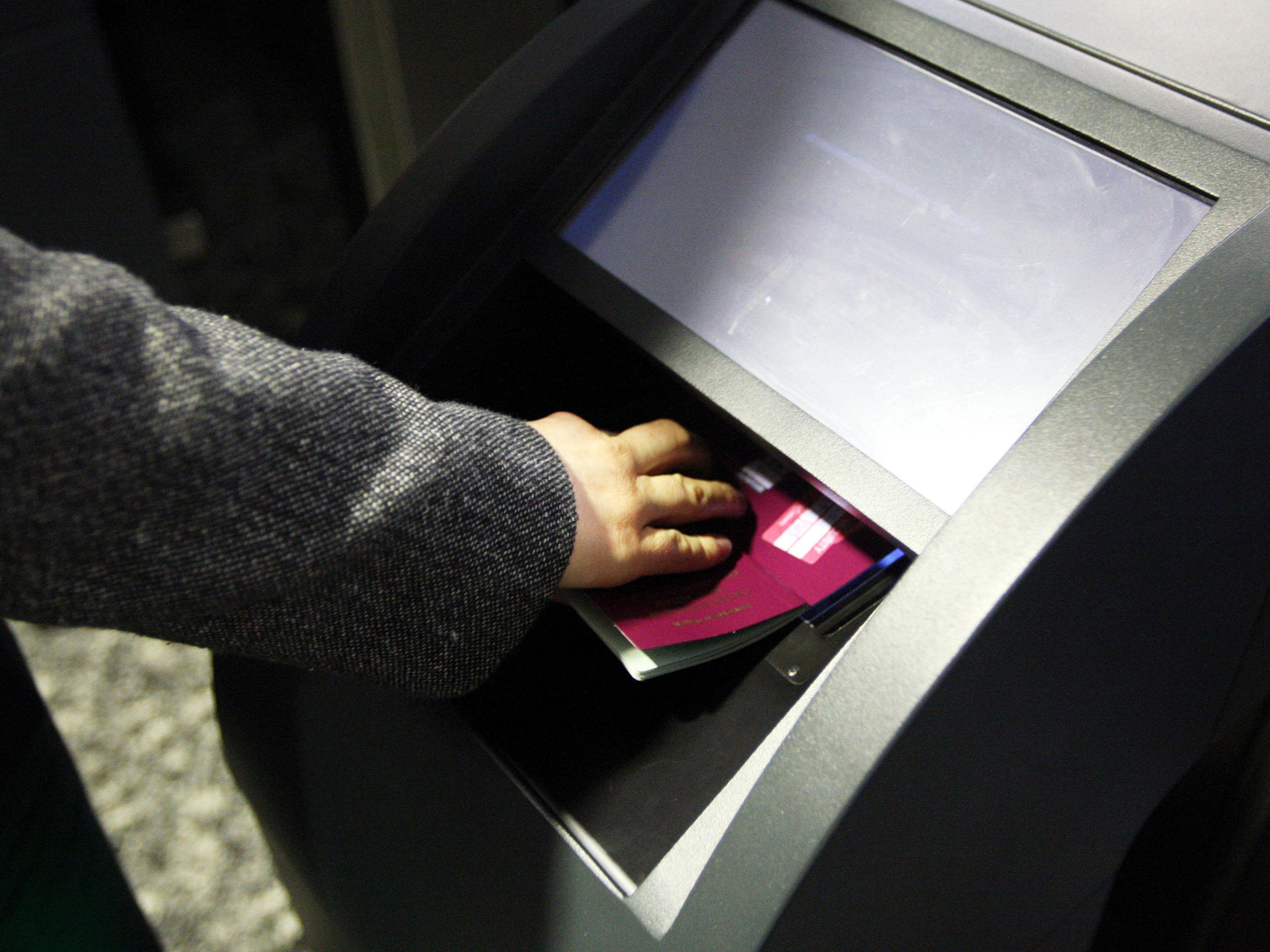 A hand holding a passport onto a scanner at an e-gate