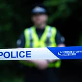 Police officer stands behind a police cordon tape