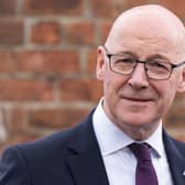 John Swinney smiling in front of a brick wall