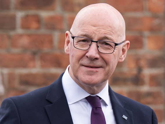 John Swinney smiling in front of a brick wall