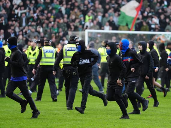 Rangers fans run on the Ibrox pitch as police form a barrier in front of Celtic supporters