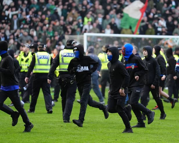 Rangers fans run on the Ibrox pitch as police form a barrier in front of Celtic supporters
