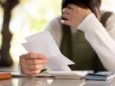 A woman with their hand on their head in distress while reading paperwork