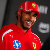 Lewis Hamilton smiling while wearing a red Ferrari jacket and cap