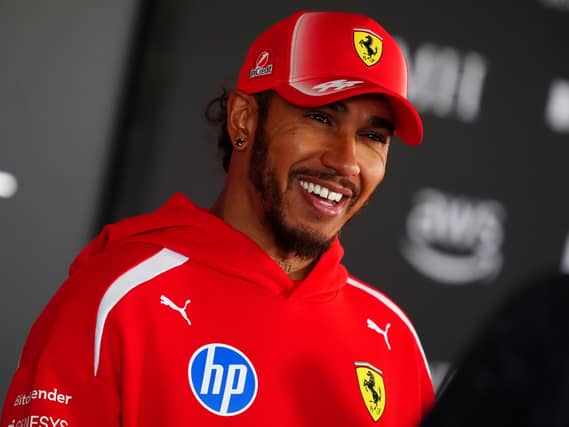 Lewis Hamilton smiling while wearing a red Ferrari jacket and cap