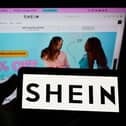 A phone with the Shein logo held in front of the website's homepage