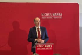 Michael Marra speaking in front of a red screen with his name on it