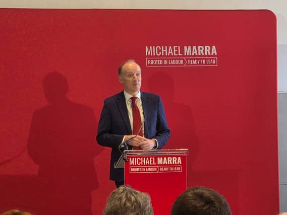 Michael Marra speaking in front of a red screen with his name on it