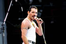 Freddie Mercury wearing a white tank and jeans holding a microphone on stage at Live Aid