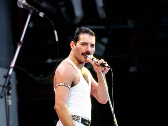 Freddie Mercury wearing a white tank and jeans holding a microphone on stage at Live Aid