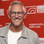 Gary Lineker wearing a white T-shirt and grey jacket smiling in front of a red banner promoting the Edinburgh TV Festival