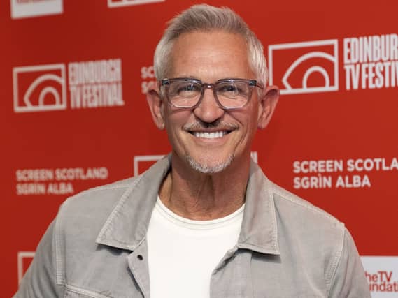 Gary Lineker wearing a white T-shirt and grey jacket smiling in front of a red banner promoting the Edinburgh TV Festival