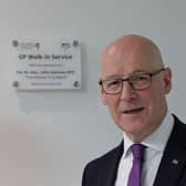 John Swinney smiling in front of a plaque on a wall