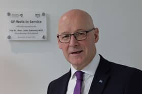 John Swinney smiling in front of a plaque on a wall