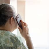 An elderly lady standing nearby the window and talking to family on the phone at bedroom in the morning. Back view, copy space.