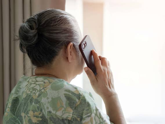 An elderly lady standing nearby the window and talking to family on the phone at bedroom in the morning. Back view, copy space.