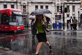 A woman steps over a puddle as she crosses a road in the rain, with a red London bus in the background