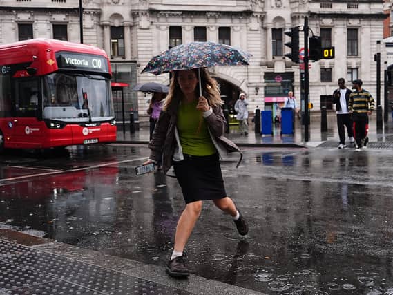 A woman steps over a puddle as she crosses a road in the rain, with a red London bus in the background