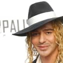 John Galliano wearing a black and white hat and black jacket with white scarf.