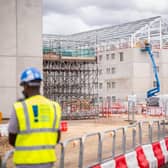 A person in a high-vis jacket and helmet with a prison construction site in the background