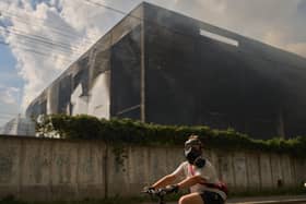 A local resident wears a gas mask as he rides a bicycle past a partially destroyed warehouse after a Russian drone attack in Brovary on the outskirts of Kyiv