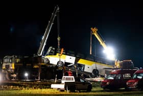 The bus is lifted by crane at the crash site during the night