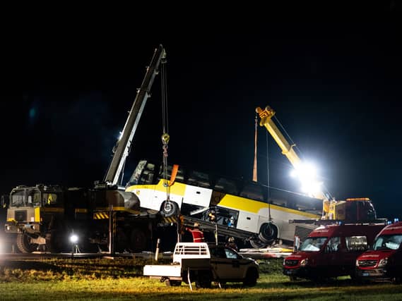 The bus is lifted by crane at the crash site during the night