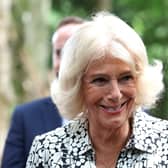 Queen Camilla smiling holding her hands together wearing a green and white shirt dress