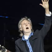 Sir Paul McCartney on stage holding a guitar and waving