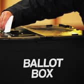A person posting their voting slip into a black ballot box